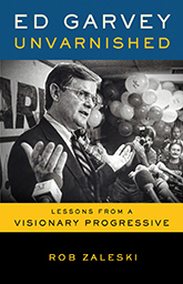 Ed Garvey Unvarnished: Cover showing a black and white photograph of Ed Garvey wearing a suit and tie giving a speech in front of a row of microphones. Behind him, a group of people can be seen, one of whom is holding a camera up to his face, taking a picture of Garvey, and behind them is a bunch of balloons.