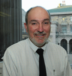 this is a photo of James P. Danky. He has a short beard and is wearing a white shirt and dark tie. Behind him is seen a pillar and a classical courtyard.